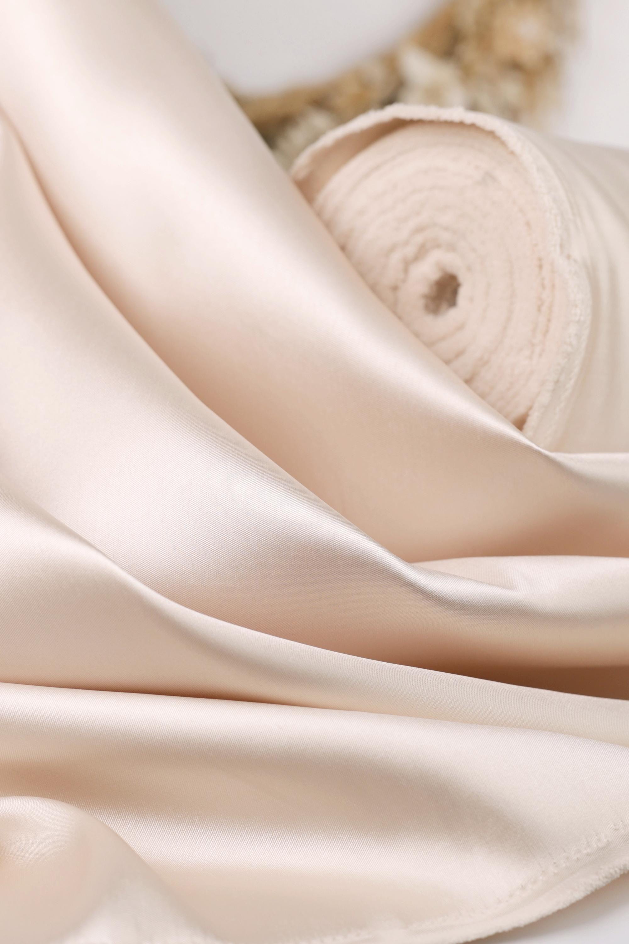 A close-up image of a soft, light pink satin fabric, possibly silk or satin, with a curled and folded appearance.