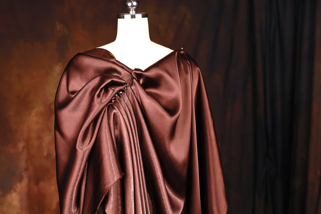 A mannequin wearing a brown satin dress with a draped, flowing design.