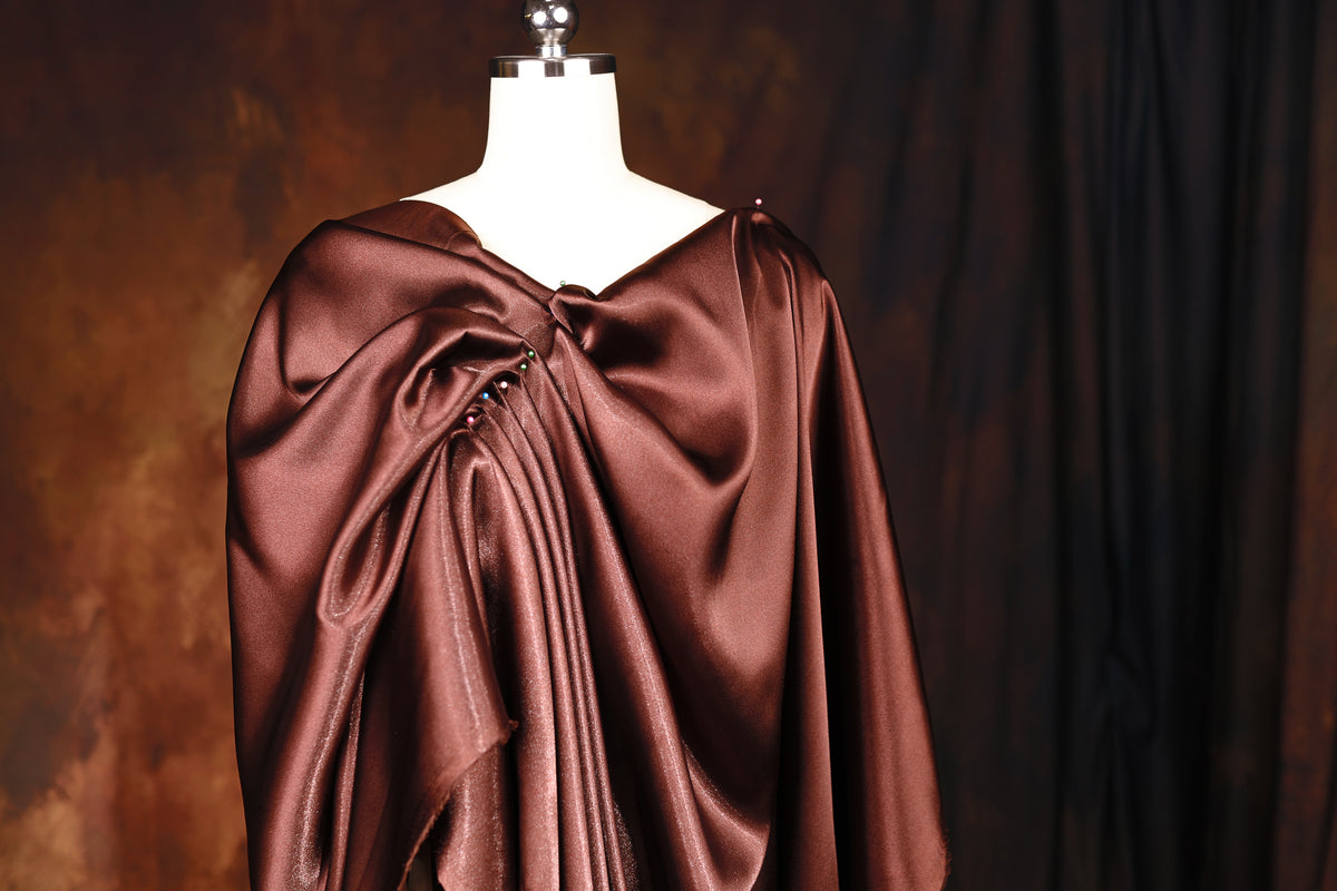 A mannequin wearing a brown satin dress with a draped, flowing design.
