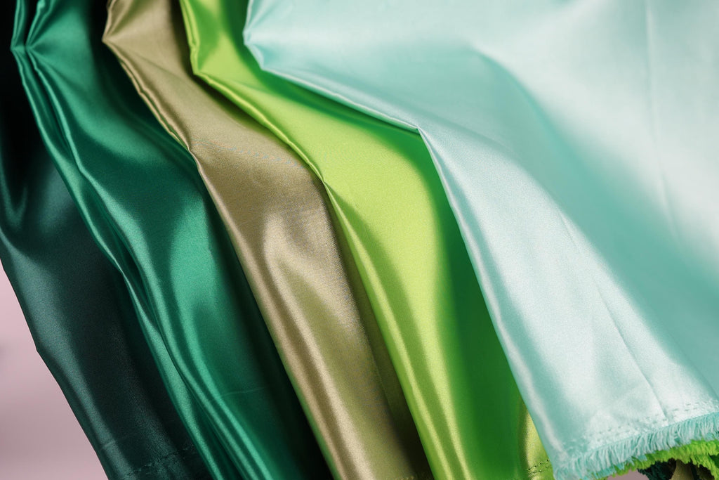 a close-up view of a collection of colorful satin fabric, with a focus on the vibrant green and gold colors.