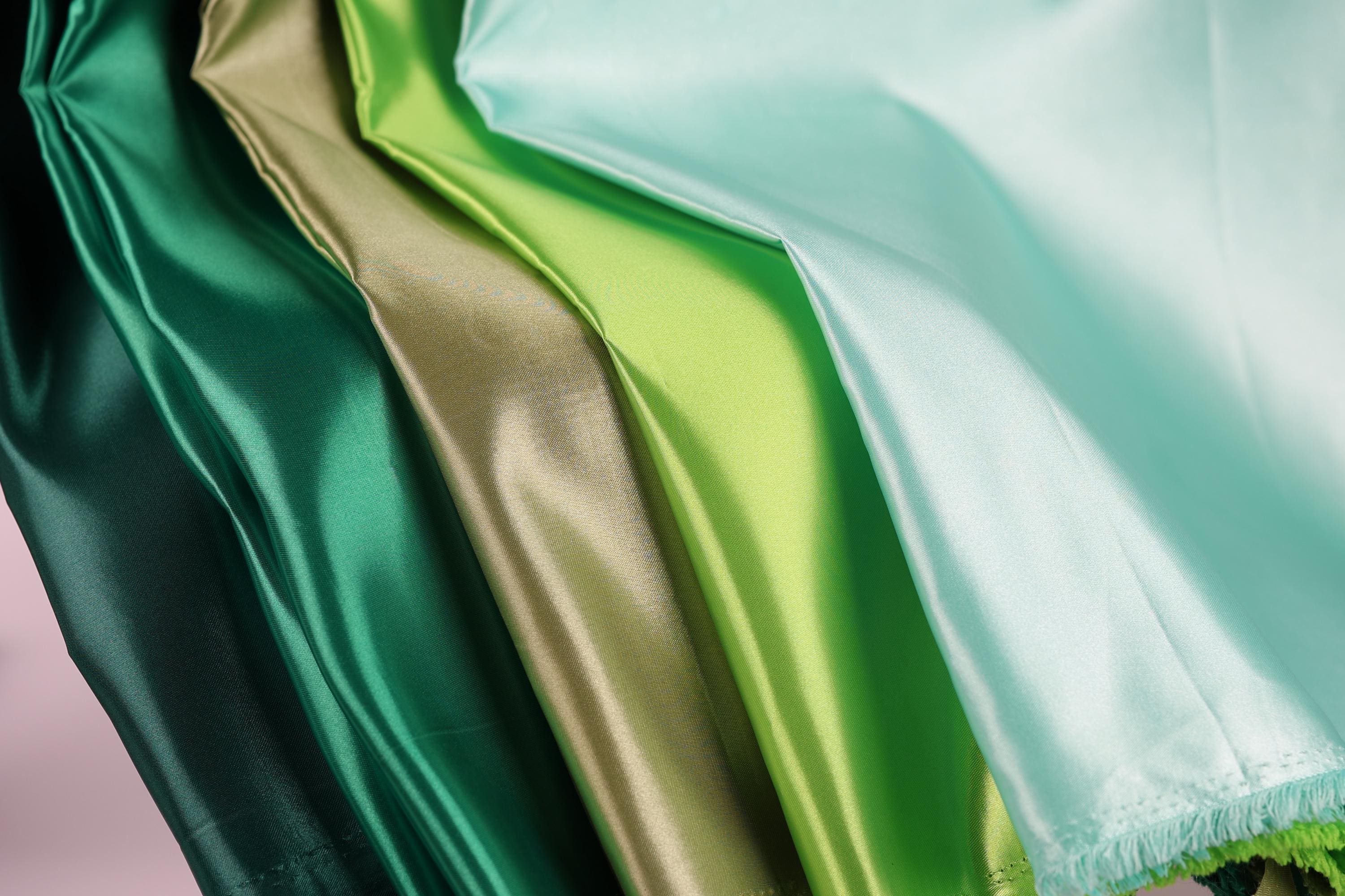 a close-up view of a collection of colorful satin fabric, with a focus on the vibrant green and gold colors.