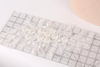 a close-up view of a delicate, white lace flower on a ruler, with a light pink background.