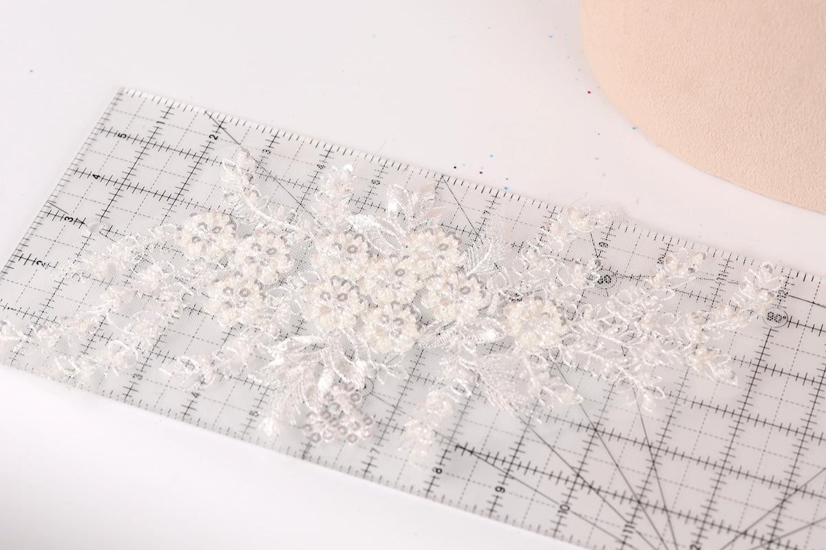 a close-up view of a delicate, white lace flower on a ruler, with a light pink background.