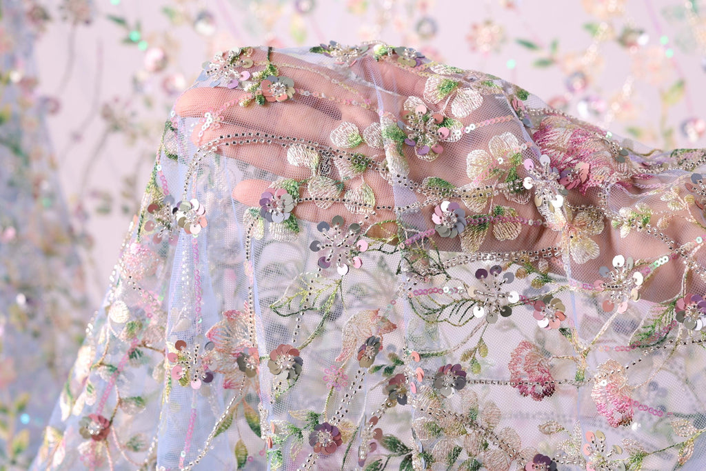 A close-up view of a hand holding a delicate, intricately embroidered fabric with a floral pattern.