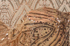 a close-up view of a fabric with a gold and black sequined pattern, featuring a repeating diamond-shaped motif.
