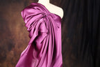 A mannequin wearing a vibrant purple one-shoulder dress with a flowing, draped design.