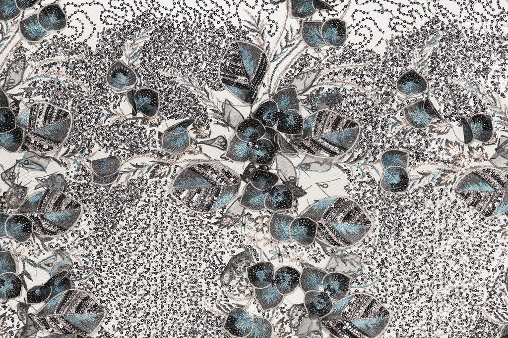 The image is a close-up of a fabric with a floral pattern, featuring a variety of blue and gray colors and intricate designs.