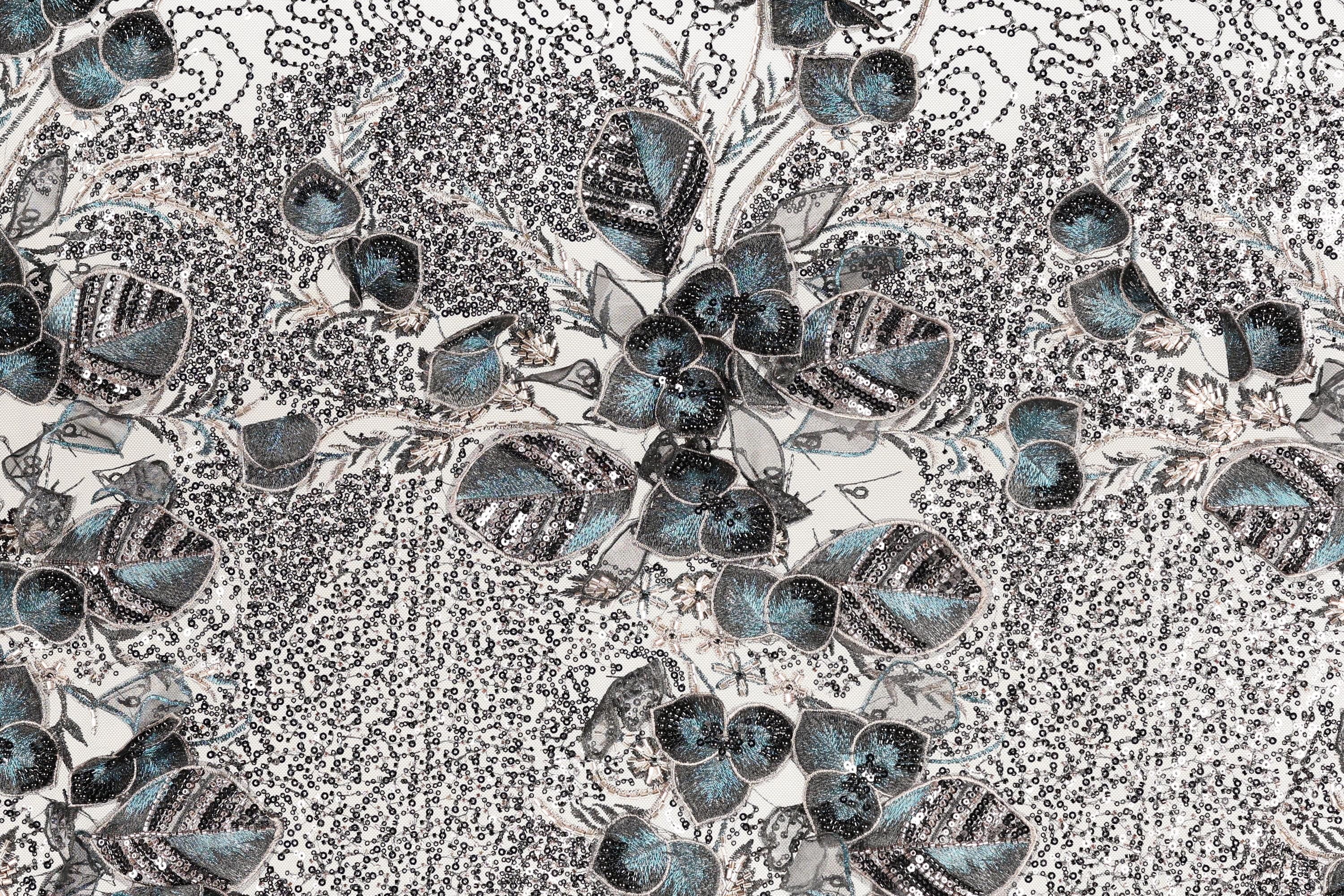 The image is a close-up of a fabric with a floral pattern, featuring a variety of blue and gray colors and intricate designs.