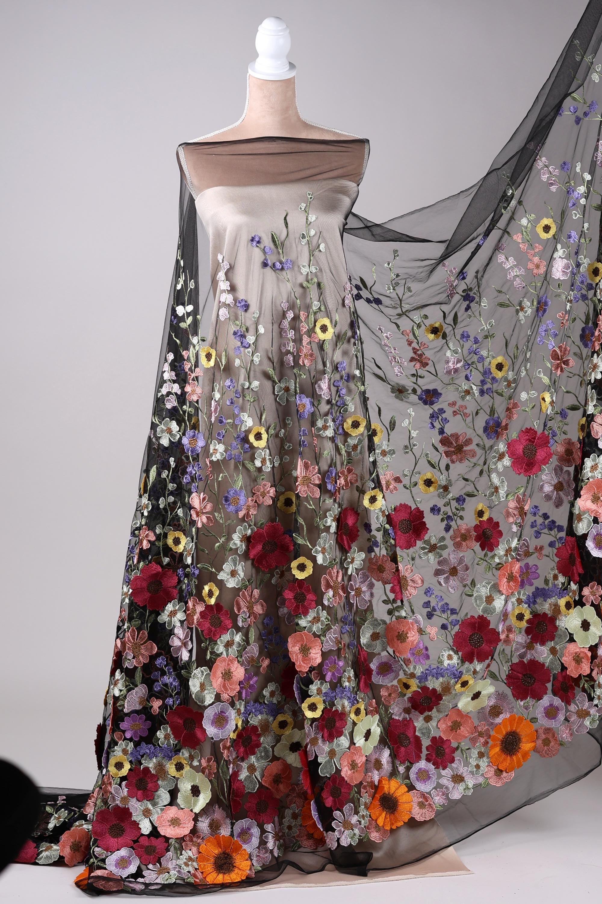 A mannequin wearing a long, flowing dress with a sheer overlay featuring a vibrant floral pattern in various colors, including red, orange, yellow, and purple.
