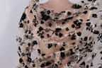 a close-up view of a delicate, sheer fabric with a floral pattern. The fabric appears to be made of sheer material, giving it a delicate and airy appearance. The floral pattern consists of black flowers interspersed with white flowers, creating a visually striking contrast against the light background. The fabric is draped over the back of a person, adding an elegant and feminine touch to the image.