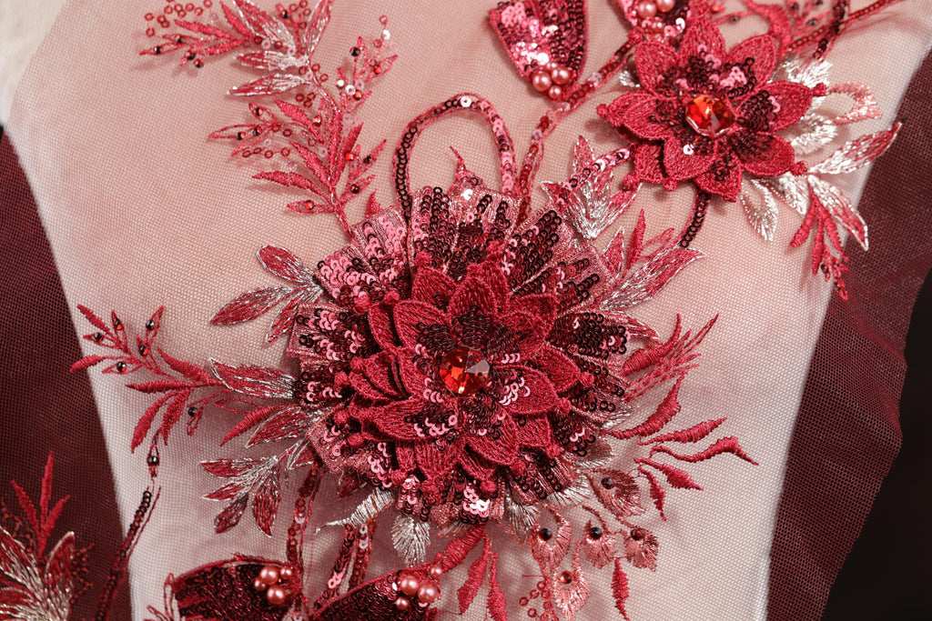 a close-up view of a red and pink floral embroidered design on a fabric, with intricate details and embellishments.