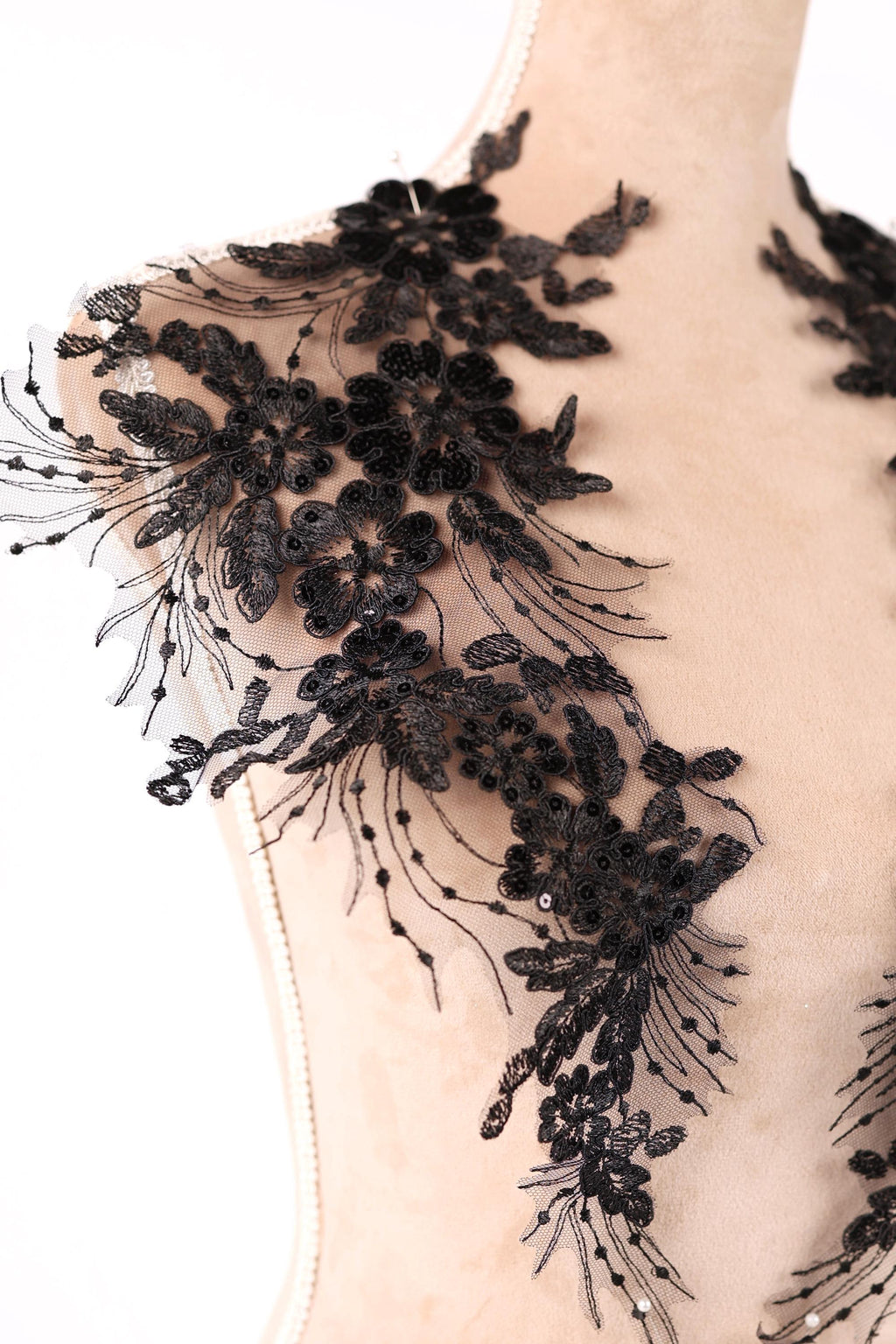 A mannequin wearing a black lace dress with intricate floral patterns and embellishments.