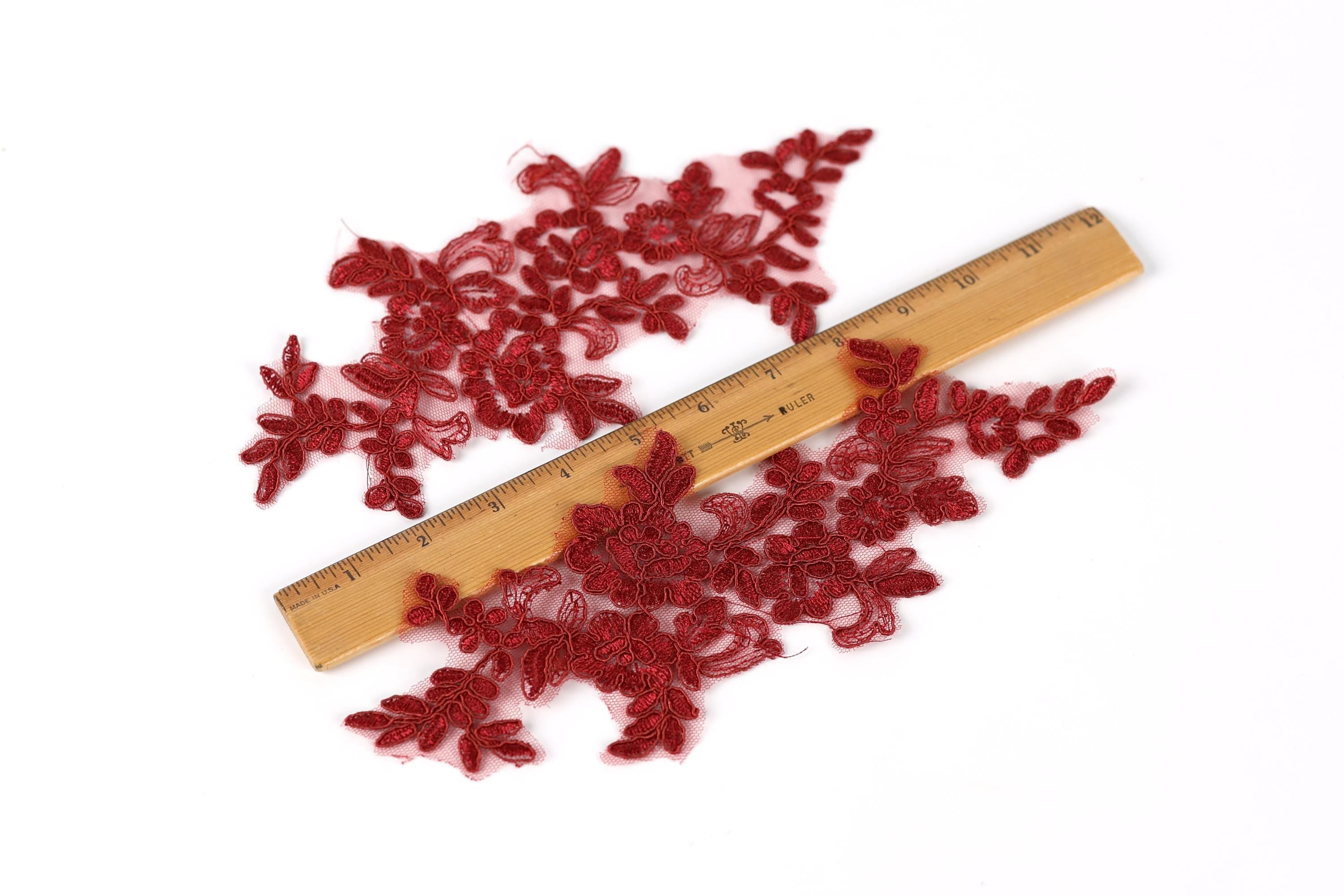 a collection of red embroidered fabric pieces, some of which are placed on a wooden ruler for size comparison.