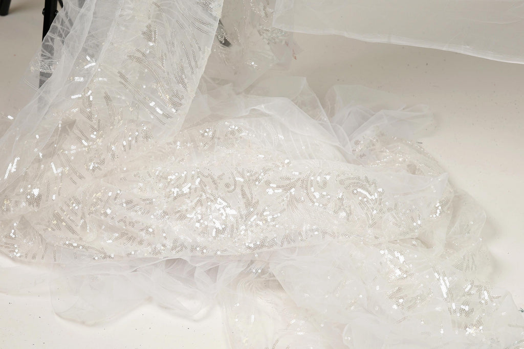 a close-up view of a delicate, white, sequined fabric, possibly a wedding dress or a similar type of garment.