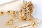 a collection of delicate, golden-colored flowers and embellishments, including a large, intricately designed flower-shaped object with numerous small flowers attached to it. The flowers are arranged on a beige fabric, creating a visually appealing and elegant display.