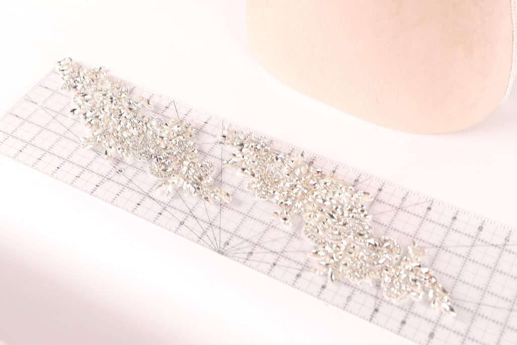 a piece of fabric with a decorative beaded or sequined design, placed on a ruler for scale.