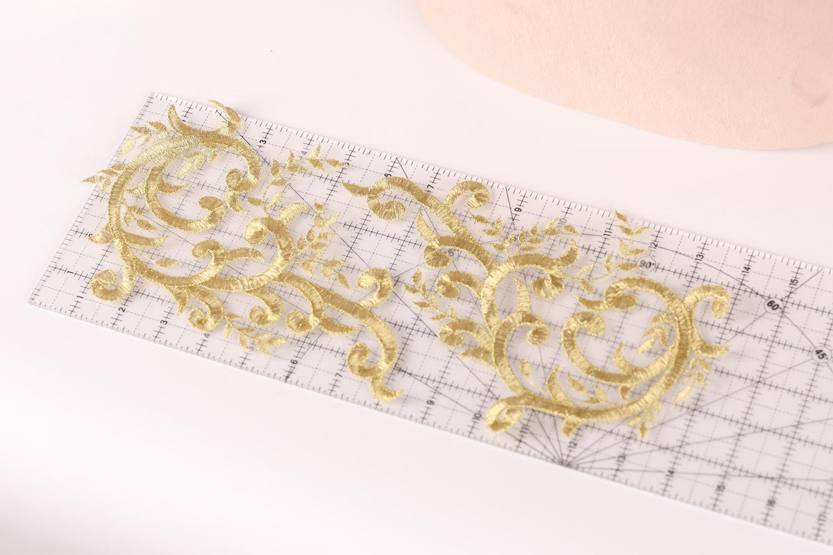 a close-up view of a ruler with gold embroidered designs on it, placed on a white surface.