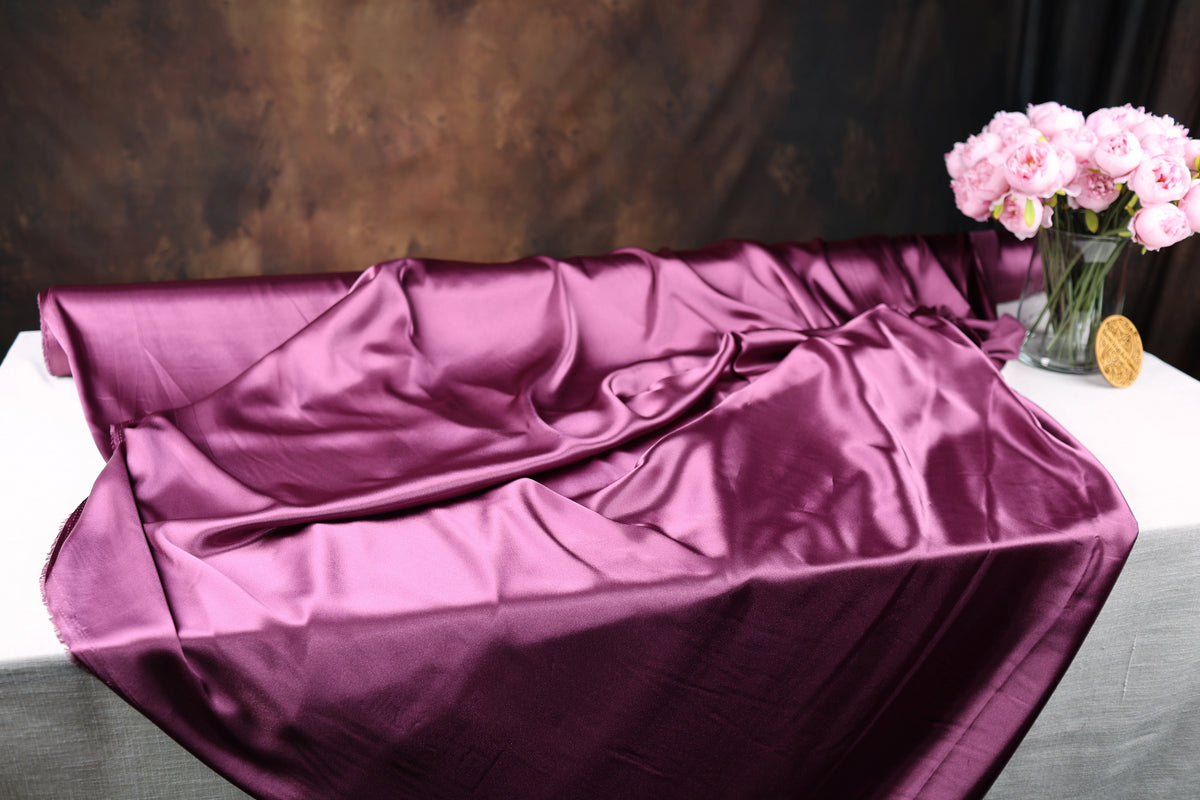a purple satin fabric draped over a table, with a vase of pink flowers placed next to it.
