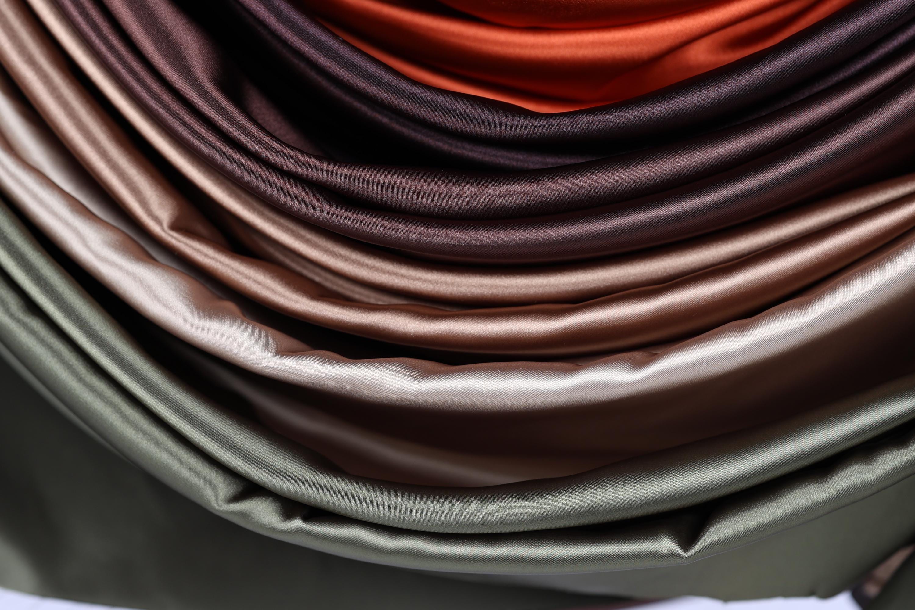 A close-up view of a pile of colorful satin fabric, with various shades of brown, orange, and green.