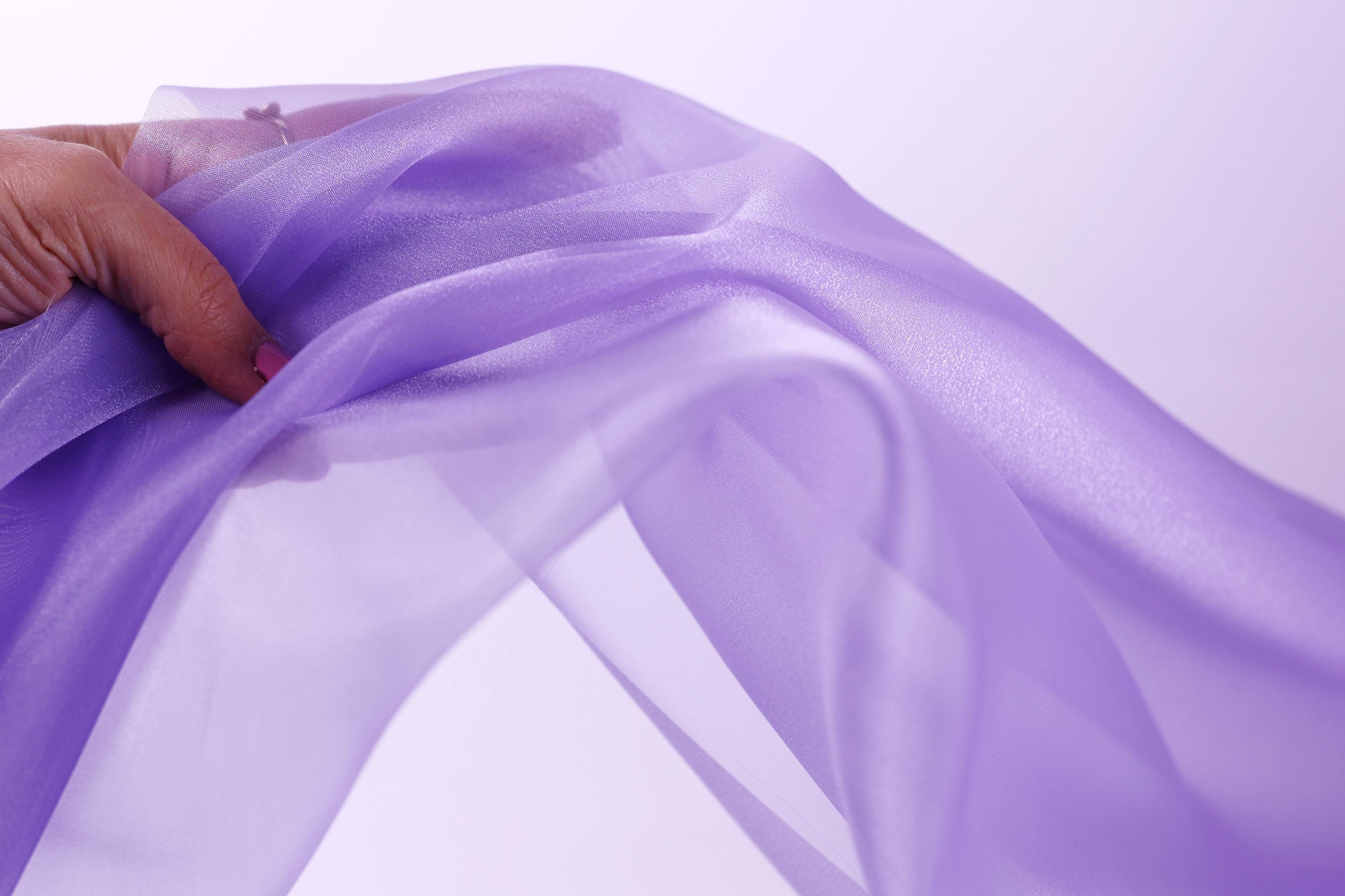 A hand is holding a piece of purple fabric, which appears to be flowing and soft.
