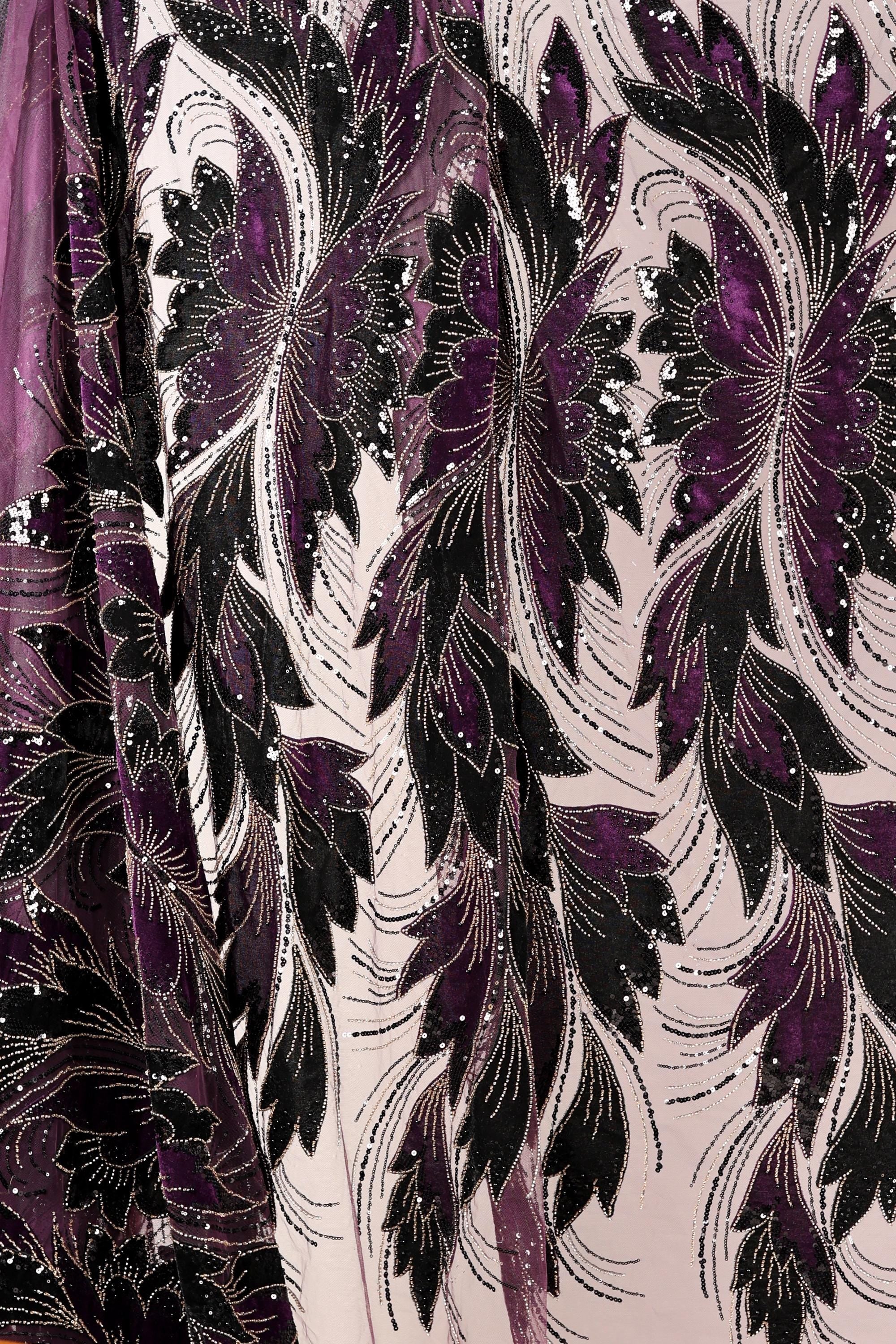 a close-up view of a fabric with a floral pattern in shades of purple and black. The fabric appears to be made of a shiny, sequined material, giving it a luxurious and elegant appearance.