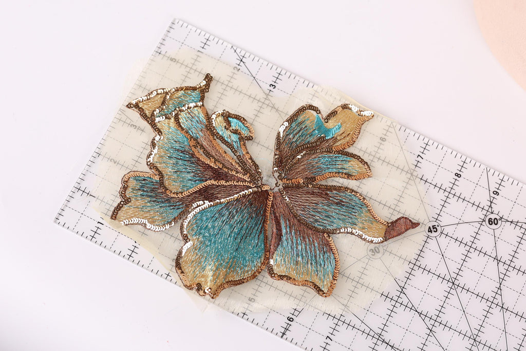 a close-up view of a detailed embroidered flower design on a transparent surface, with a ruler for scale.