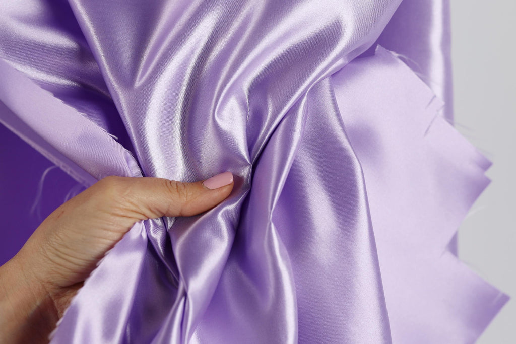 A hand is holding a piece of purple satin fabric, with the fabric being folded and twisted.