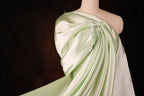 A mannequin wearing a flowing, green satin dress with a draped, flowing silhouette.