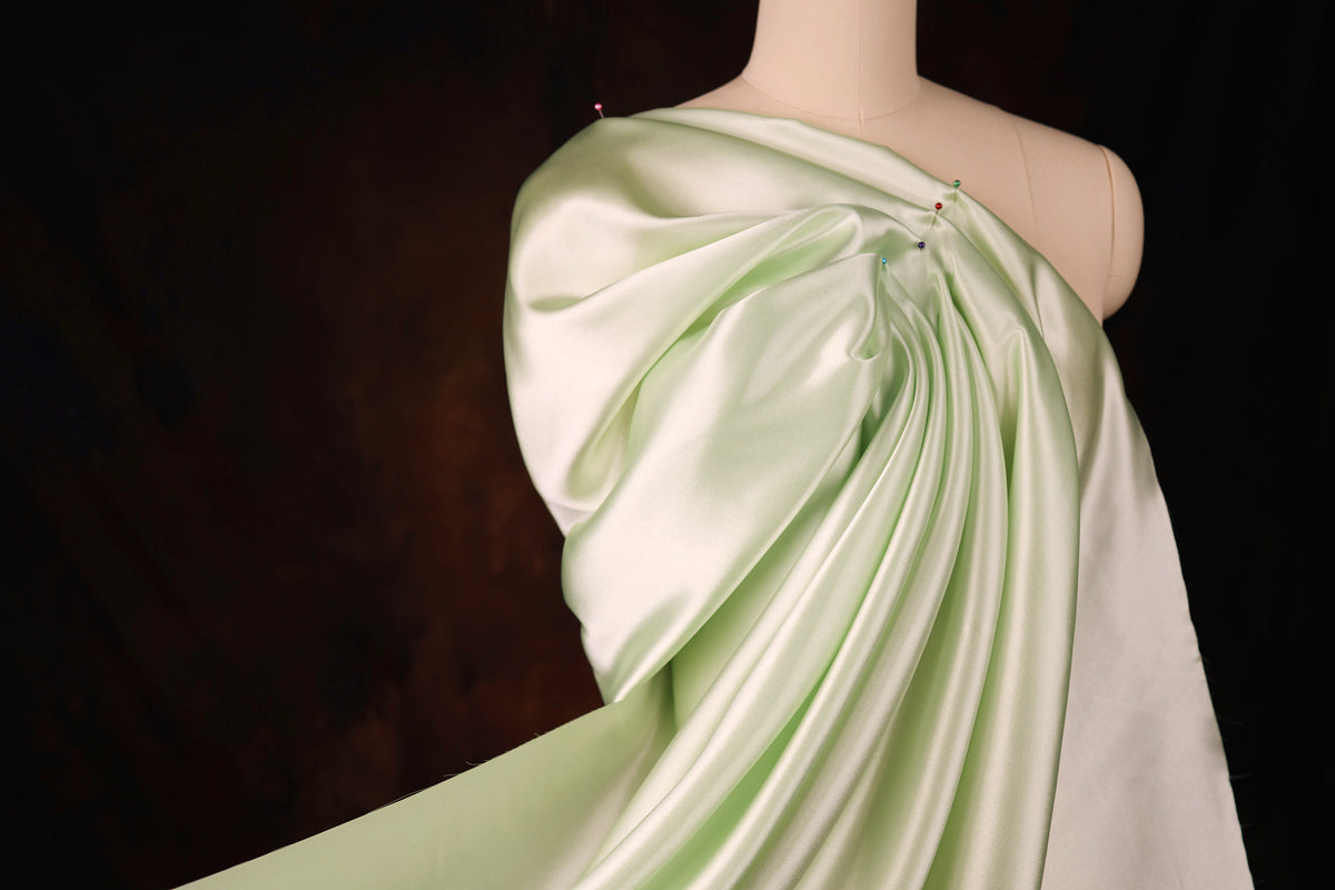 A mannequin wearing a flowing, green satin dress with a draped, flowing silhouette.