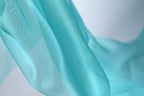 A close-up view of a flowing, turquoise-colored fabric, with a blurred background that emphasizes the fabric's texture and movement.