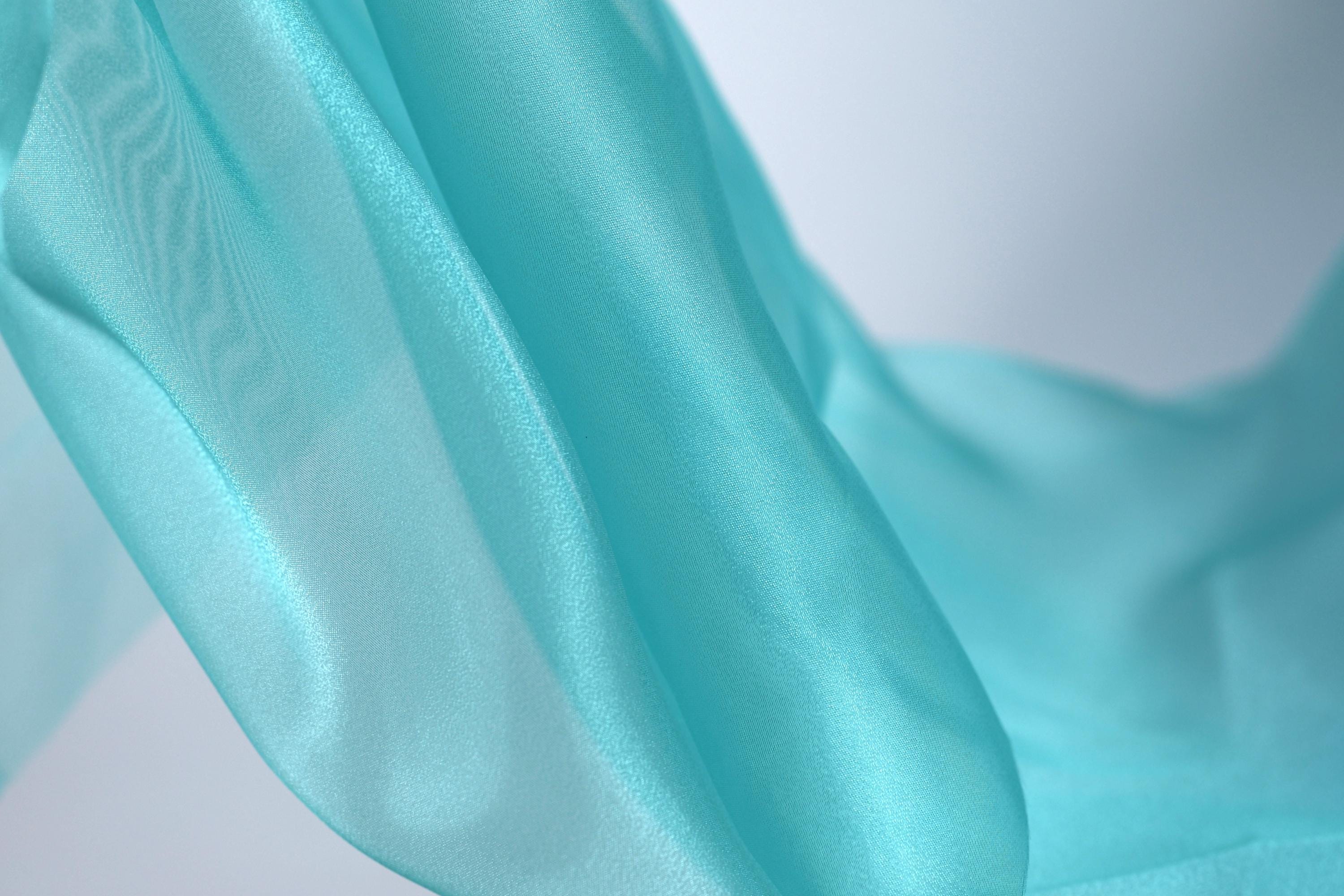 A close-up view of a flowing, turquoise-colored fabric, with a blurred background that emphasizes the fabric's texture and movement.