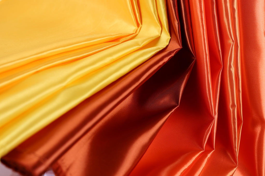 a close-up view of a fabric with a vibrant mix of yellow, orange, and red colors. The fabric appears to be made of a shiny, shiny material, giving it a textured and visually striking appearance.