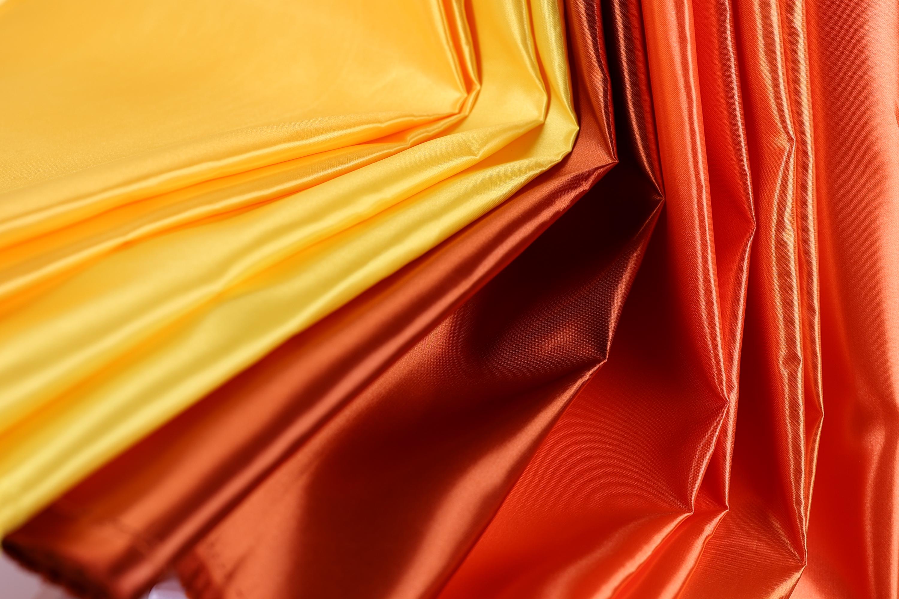 a close-up view of a fabric with a vibrant mix of yellow, orange, and red colors. The fabric appears to be made of a shiny, shiny material, giving it a textured and visually striking appearance.