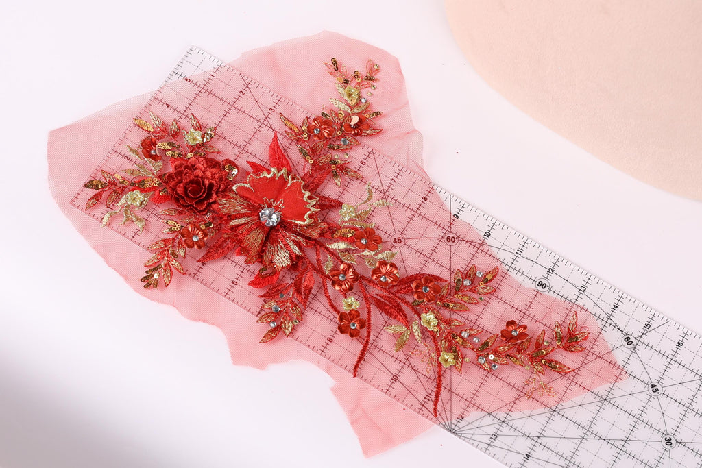 a close-up view of a red floral embroidery piece with gold accents, placed on a pink background.