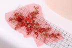 a close-up view of a red floral embroidery piece with gold accents, placed on a pink background.
