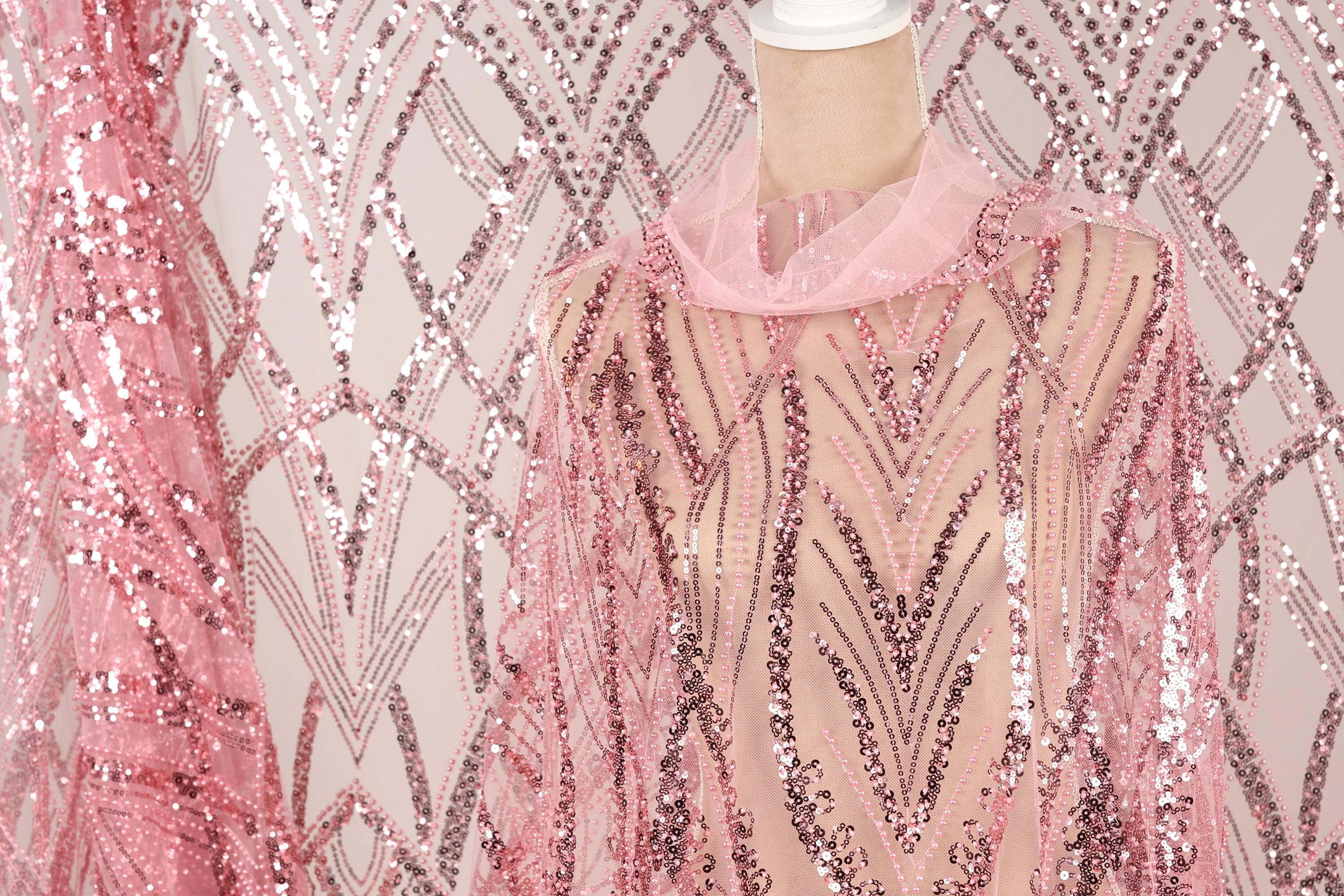 a mannequin wearing a pink sequin dress with a sheer overlay. The dress has a pink and silver sequin pattern, creating a visually striking and elegant design.