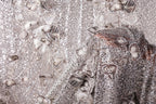 The image is a close-up of a fabric with a silver sequin pattern, featuring a variety of shapes and textures.