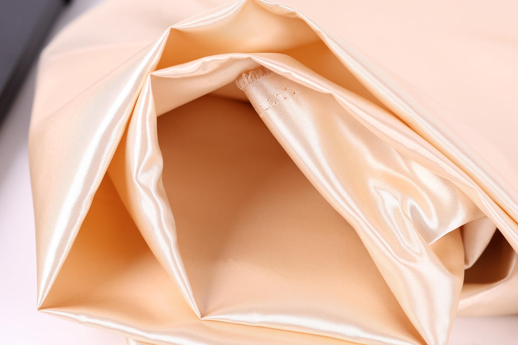 A close-up view of a soft, light-colored fabric, possibly silk or satin, with a smooth, shiny texture.
