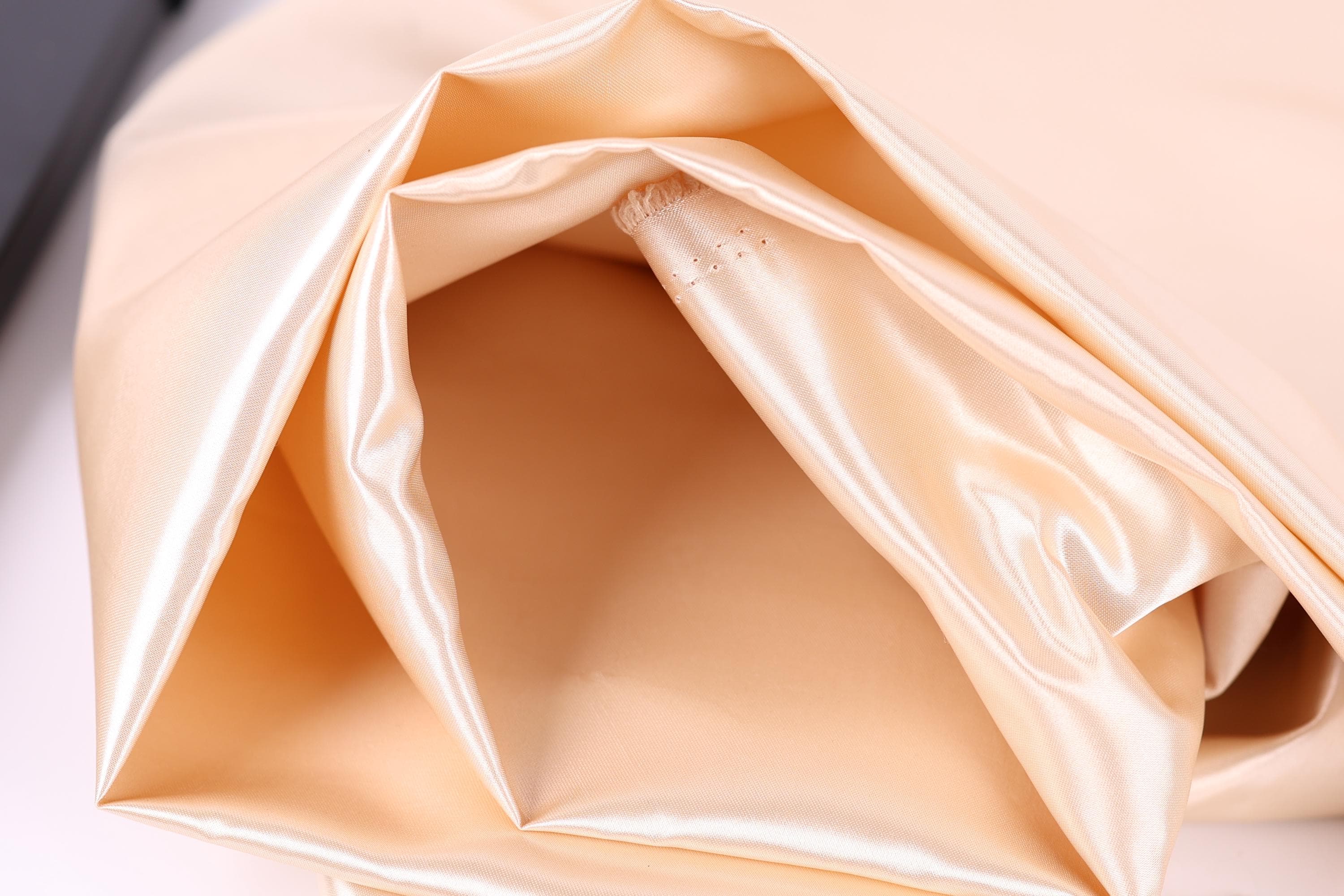 A close-up view of a soft, light-colored fabric, possibly silk or satin, with a smooth, shiny texture.