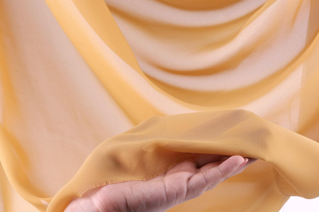 A hand is holding a piece of yellow fabric, which appears to be a soft, flowing material.