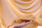 A hand is holding a piece of yellow fabric, which appears to be a soft, flowing material.