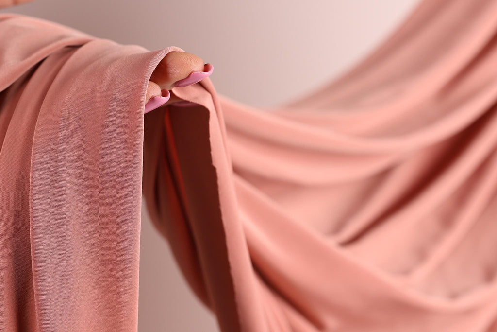 A close-up view of a pink fabric, possibly a sheer or sheer-like material, with a person's hand visible on the left side.