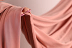 A close-up view of a pink fabric, possibly a sheer or sheer-like material, with a person's hand visible on the left side.