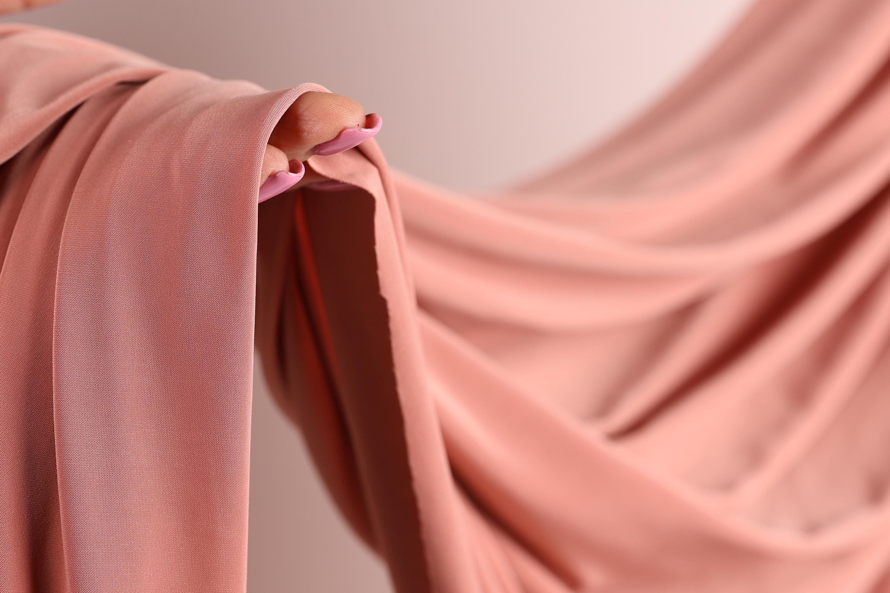 A close-up view of a pink fabric, possibly a sheer or sheer-like material, with a person's hand visible on the left side.