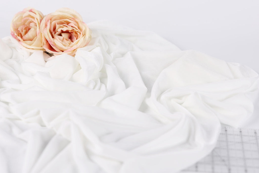 two pink roses resting on a white fabric surface.