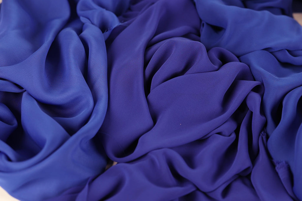 The image is a close-up of a crumpled, blue fabric, possibly silk or chiffon, with a textured and wrinkled appearance.