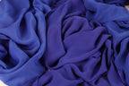 The image is a close-up of a crumpled, blue fabric, possibly silk or chiffon, with a textured and wrinkled appearance.