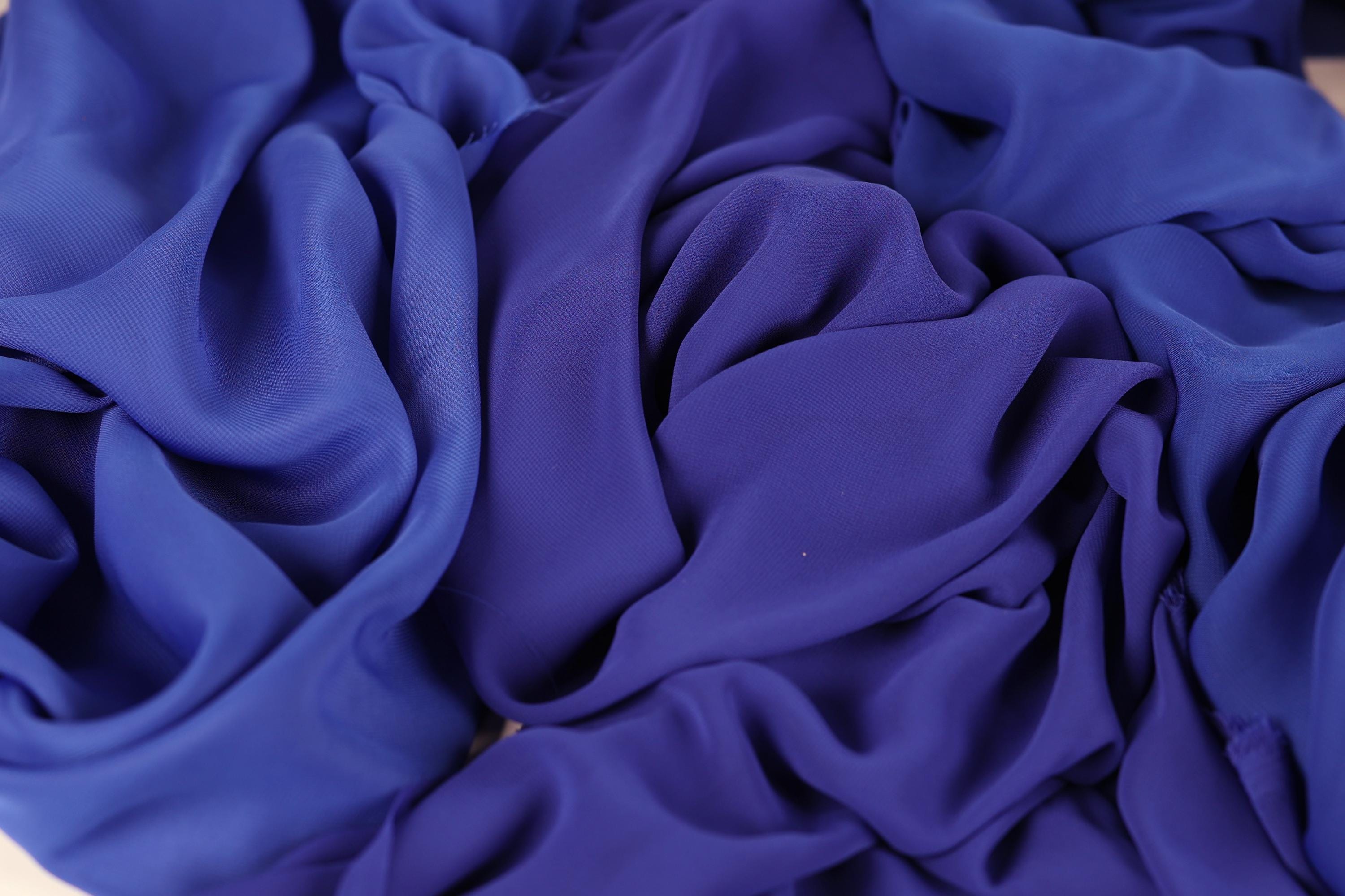 The image is a close-up of a crumpled, blue fabric, possibly silk or chiffon, with a textured and wrinkled appearance.