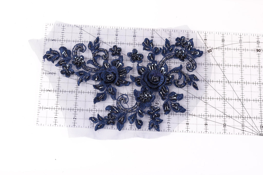 a close-up view of a piece of fabric with a floral design, including blue flowers and leaves. The fabric is placed on a transparent ruler, which is lying on a white surface.