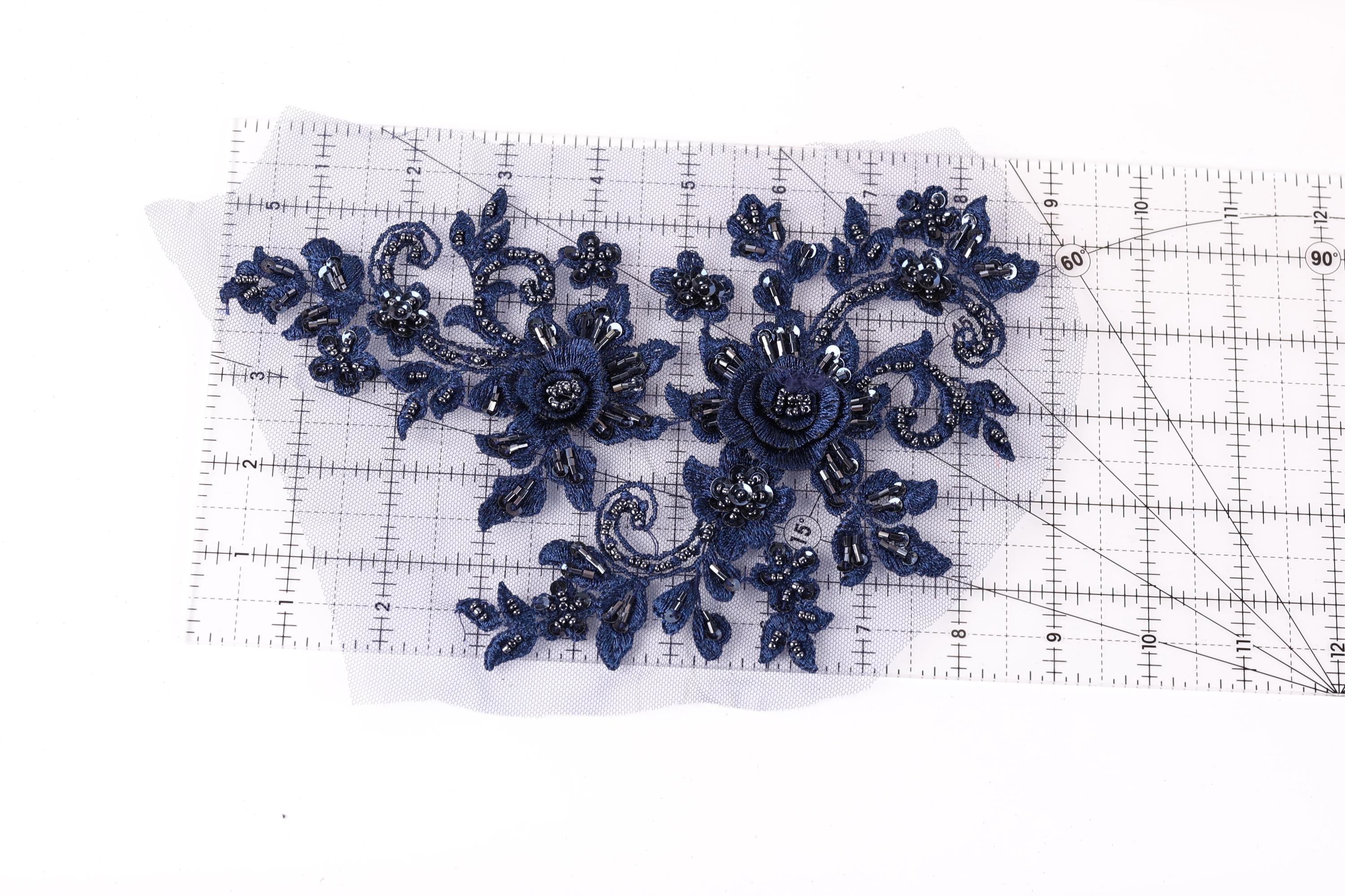 a close-up view of a piece of fabric with a floral design, including blue flowers and leaves. The fabric is placed on a transparent ruler, which is lying on a white surface.